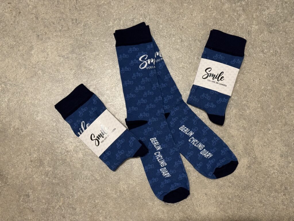 Drei Paar blaue Socken mit Fahrradmuster und der Aufschrift "Smile You are on camera" und "Berlin Cycling Diary".